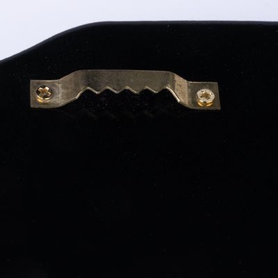 Close-up of a gold-coloured metal hanger with a serrated edge, attached to a black surface.