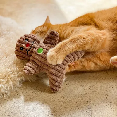 Bruin stoffen speelgoed in de vorm van een boom met rode en groene accenten, vastgehouden door een kat.