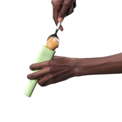 Mano tiene un gioco di gomma verde con texture mentre un cucchiaio spalma burro di arachidi sopra.