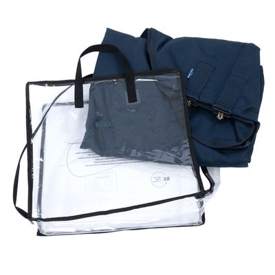 Sac de transport transparent avec poignées noires, pochette bleue visible portant le texte 'NOMAD TALES', tissu bleu plié avec fermetures éclair métalliques.