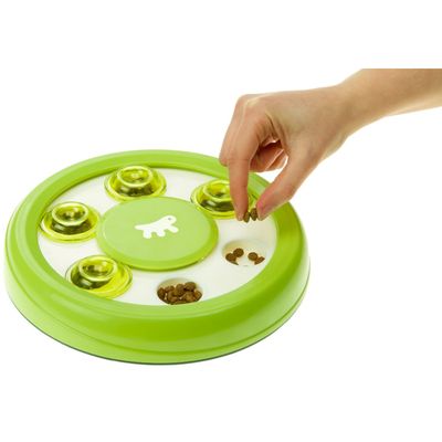 Zielona interaktywna zabawka na karmę z kilkoma komorami, wypełniona suchą karmą. Ręka podnosi pokrywkę, aby pokazać dostęp do karmy.