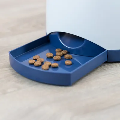 Automatische voerdispenser met blauwe schaal, gevuld met bruine brokjes droogvoer.