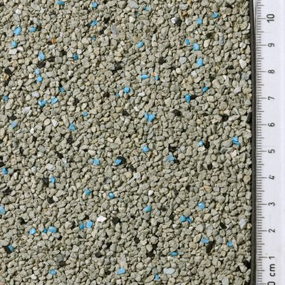 Close-up van grijs granulaat met blauwe deeltjes, daarnaast een liniaal voor maatindicatie in centimeters.