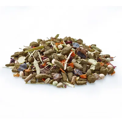 Mélange d’aliments pour petits animaux, composé de granulés, morceaux de légumes séchés et herbes visibles, présenté en vrac sur fond blanc.