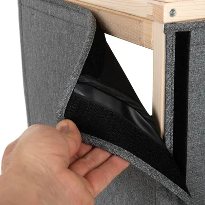 Hånd viser gråt stof med velcrolukning på en træramme, aftagelig for nem rengøring.