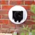A black cat using a white pet door installed in a brick wall, demonstrating the product's function for allowing pets to pass through walls.