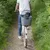 Panier arrière pour vélo en plastique gris avec grille métallique, contenant un petit chien noir, fixé sur le porte-bagages d’un vélo blanc conduit par une personne en jean et t-shirt blanc.