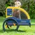 Yellow-blue dog trailer with mesh window and the inscription 'Hafenbande', dog sitting inside. Trailer with two wheels and reflectors, suitable for bicycles.