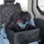 Hund in einem schwarzen Autositz mit Sicherheitsgurt und farbigem Geschirr. Sitz mit gesteppter Rückenlehne und blauer Decke im Auto.