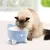 Gato a beber de uma fonte de água azul em forma de gato com patas e bigodes brancos. Produto mostra o uso da fonte para animais de estimação.