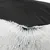 Detalle de la base antideslizante negra con puntos y borde de pelo sintético blanco de una cama para mascotas.
