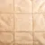 Detalle de superficie acolchada de tela beige con costuras visibles formando cuadrados. Material textil suave, adecuado para productos como camas o mantas para mascotas.