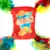 Jouet en tissu rouge avec l’inscription « CRISPS » et des illustrations de chips, décoré de plumes vertes, bleues, jaunes et rouges aux quatre coins. Texte anglais visible.