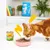 Oranje-witte kat eet natvoer uit roze bakje. Twee blikjes kattenvoer zichtbaar: geel met tekst 'DINDE ET POULET', groen met tekst 'AGNEAU ET POULET'.