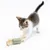 Chaton jouant avec un jouet cylindrique en tissu vert à motif quadrillé, décoré de plumes beiges aux extrémités. Jouet et chat visibles sur fond blanc.