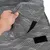 Nahaufnahme eines grauen, gemusterten Stoffbezugs mit Klettverschluss, der von einer Hand angehoben wird.