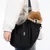 Tiaki black carrier bag with quilted design, dog sitting inside. Adjustable shoulder strap and mesh details visible.