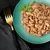 Chunks of wet pet food in gravy served on a green plate with a parsley garnish, shown next to a gold fork on a dark cloth napkin.