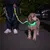 Hund mit leuchtendem grünen Halsband und Leine bei Nacht, geführt von einer Person. Sichtbarkeit im Dunkeln durch LED-Halsband.