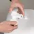 Hands showing the assembly of a white dispenser with screw cap on a container lid.