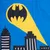 Batman symbol in yellow beam of light above a stylised skyline on blue background.