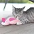 Graue Katze spielt mit rosa Plüschspielzeug in Form eines Vogels auf einer Holzterrasse.