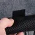 Nahaufnahme eines Klettverschlusses an einem grauen Stoff und schwarzem Netzmaterial, gehalten von einer Hand.
