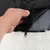Close-up van een hand die een zwarte ritssluiting opent aan een witte, pluizige hoes en de binnenvoering laat zien.
