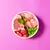 Bowl containing raw meat cuts, green peas, a mint leaf, a white tablet and a clear liquid capsule, showing key ingredients of pet food.