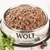 Wolf of Wilderness vådfoder i en skål af rustfrit stål, omgivet af friske ingredienser som blåbær, tranebær og mælkebøtteblade.