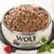 Wolf of Wilderness wet food in a stainless steel bowl, surrounded by raspberries, blueberries and fresh herbs.