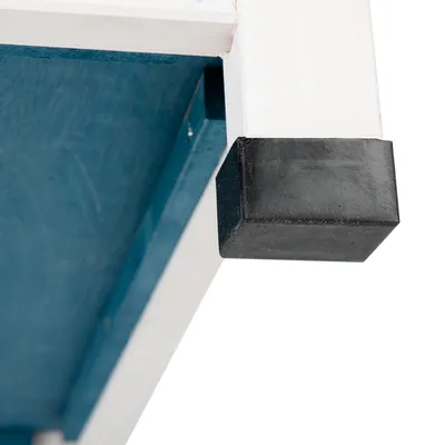 Nahaufnahme eines schwarzen Kunststoff-Fussschutzes an einem weissen Holzrahmen mit blauer Unterseite.