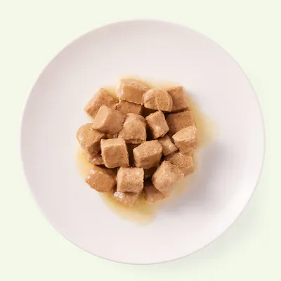 Närbild av bruna köttbitar i sås på en vit tallrik.