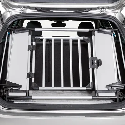 Transportbox aus Metall und Kunststoff im Kofferraum eines Autos, mit Gitterstäben und Sicherheitsverschluss.