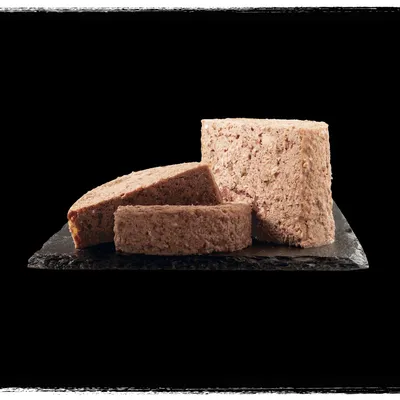 Comida húmida para animais de estimação em formato cilíndrico, cortada em fatias grossas e apresentada sobre uma base escura. Sem embalagem visível.