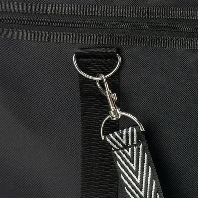 Gros plan sur une sangle en tissu noir et blanc à motif chevron, fixée par un mousqueton métallique à un anneau en métal sur un sac en tissu noir avec fermeture éclair visible.