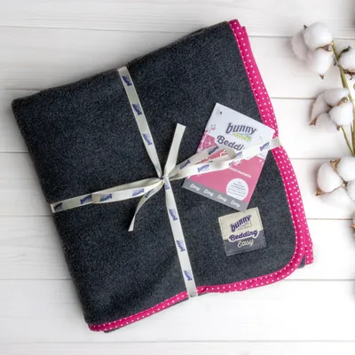 Bunny Bedding Easy, covoraș de așternut gri închis cu margine roz și design cu buline, ambalat cu bandă Bunny. Etichetă de produs și ramură de bumbac vizibile.