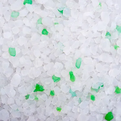 Close-up van witte korrels met enkele groene stukjes, materiaal lijkt op silicaat of kristallen. Geen merknaam of tekst zichtbaar.