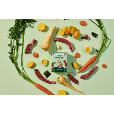 Grain free lamb pet food packaging surrounded by visible ingredients including carrots, parsnips, potatoes, eggs and meat pieces, highlighting main components of the product.