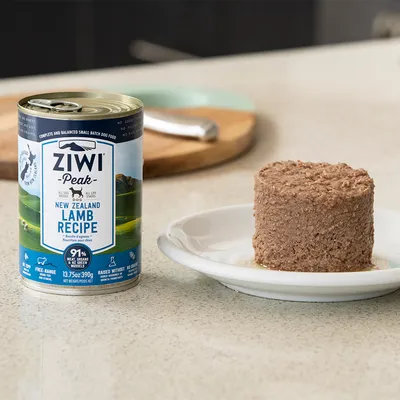 Boîte de pâtée pour chien Ziwi Peak New Zealand Lamb Recipe 390 g, posée à côté d'une portion servie sur une assiette blanche. Texte visible : 91 % viande et abats, élevage en plein air.