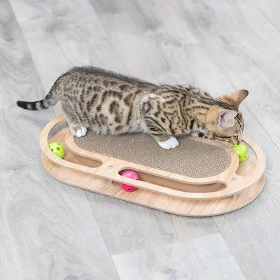 Giocattolo per gatti in legno con superficie tiragraffi e piste integrate per palline colorate. Gatto gioca attivamente con una pallina verde.