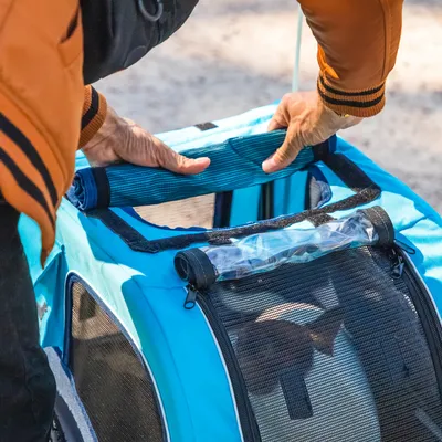 Person zeigt die Tragefunktion einer blauen Transporttasche mit Netzfenstern und gepolstertem Griff.