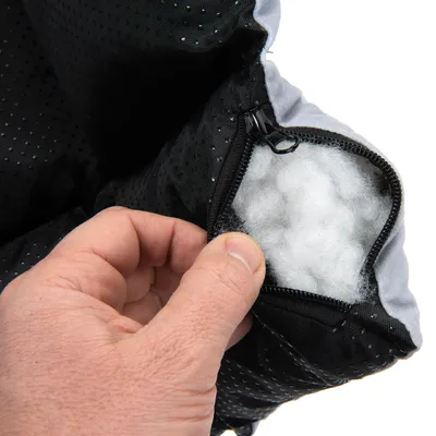 Nahaufnahme eines schwarzen Stoffbezugs mit Reissverschluss, der weisse Füllung zeigt. Hand öffnet den Bezug zur Ansicht des Innenmaterials.