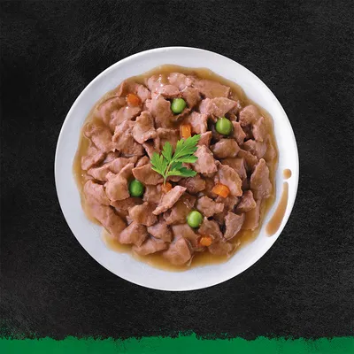 Чиния с парчета месо в сос, гарнирани със зелен грах, моркови и стрък магданоз. Видими съставки: месо, грах, морков, магданоз.