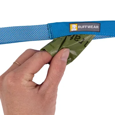 Hand pulling green bag from blue Ruffwear lead with visible Ruffwear brand label