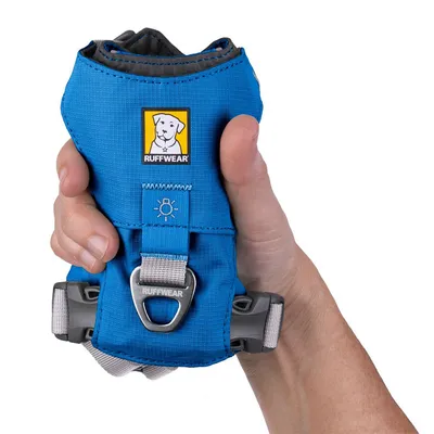 Ruffwear koiranvaljaat sinisenä, kestävä metallirengas ja heijastava symboli. Pidetään kädessä koon vertailua varten.