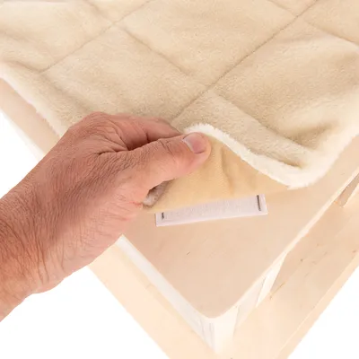 Una mano levanta una almohadilla beige y suave con cierre de velcro de una superficie de madera. Vista detallada del método de fijación.