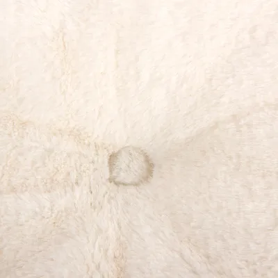 Gros plan sur une surface en tissu peluche beige avec un bouton central visible, détail d’un coussin ou panier pour animaux.