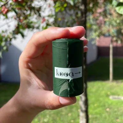 kooa. Темно-зеленый рулон, держится в руке, с логотипом kooa и стрелкой.