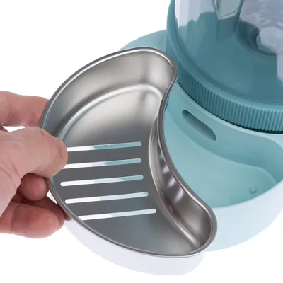 Hand hält herausnehmbaren Edelstahleinsatz mit Schlitzen, passend für einen blauen Futter- oder Wasserspender.